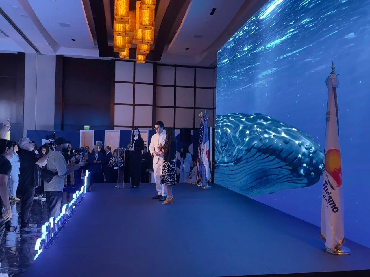Curved LED wall showing a humpback whale, flanked by vertical LED towers and illuminated Republica Dominicana lettering, at a Dominican Republic tourism showcase in Miami